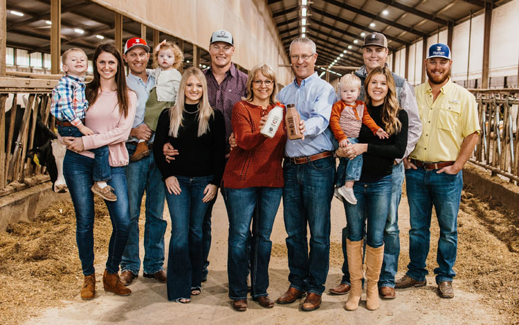 A Family of dairy farmers poses for a group photo, and the people range in age from toddler to elder.